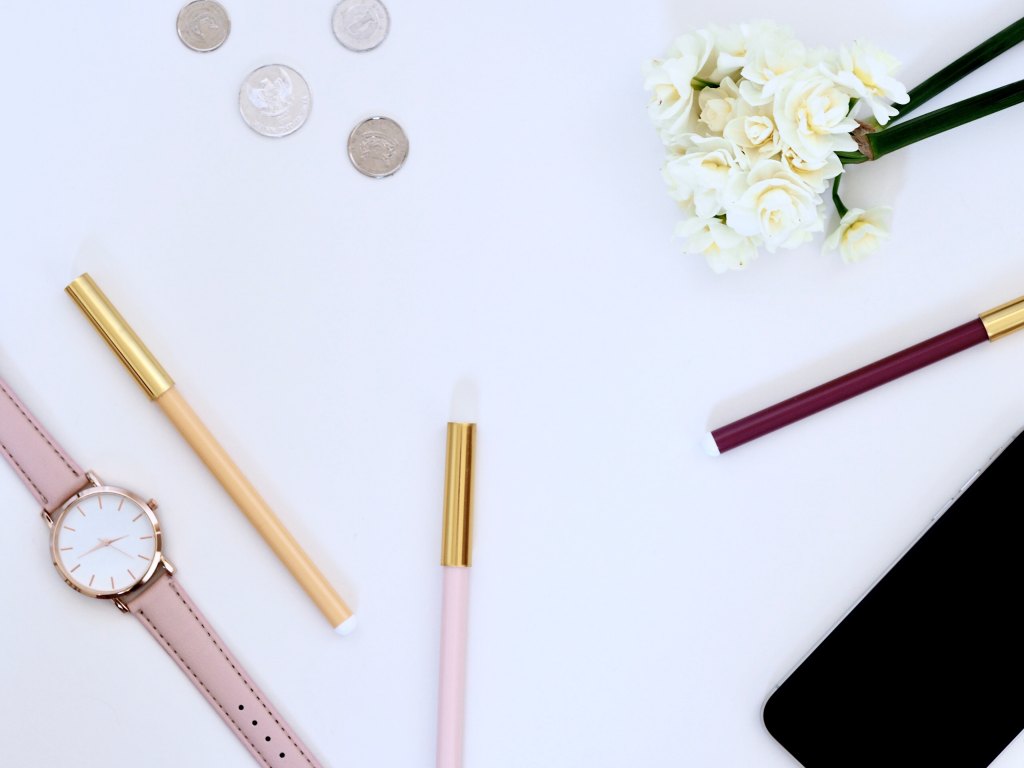 A picture of a white table top with some pink accessories and white roses artfully arranged on top. Think something that an Instagram blogger would post to show people they're being productive.